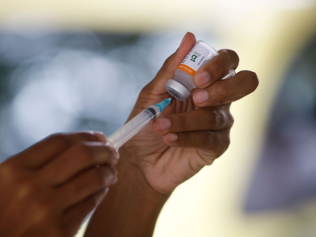 Mão de enfermeira segurando um frasco da vacina e uma seringa