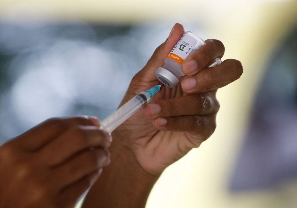 Mão de enfermeira segurando um frasco da vacina e uma seringa