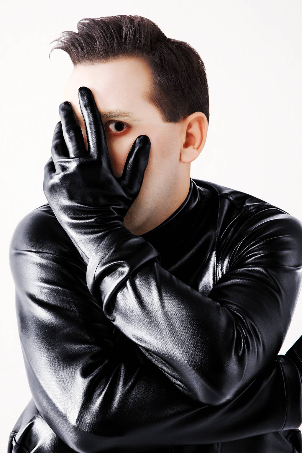Homem com roupa de couro preta com uma das mãos, de luva preta, no rosto