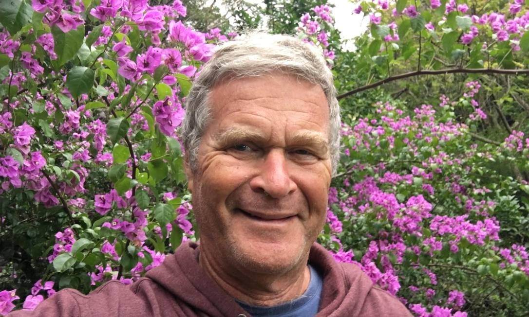 Foto mostra Alfredo Sirkis na frente de uma árvores com flores rosa