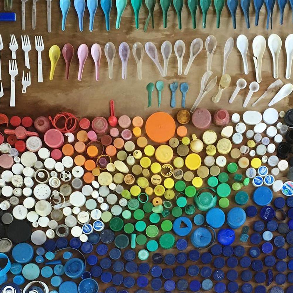 Foto mostra diversos tipos de plástico, como colheres descartáveis e tampas plásticas de diversas cores em uma mesa, uma ao lado da outra