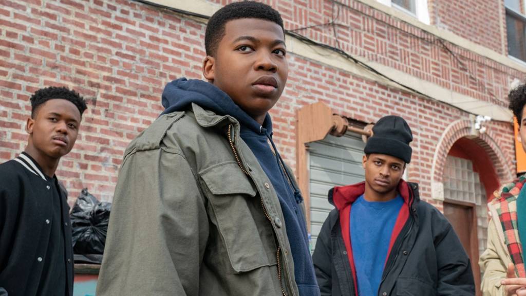 Imagem mostra grupo de adolescentes negros em frente a um prédio de tijolos