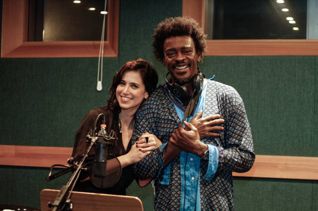 Mel Lisboa e Seu Jorge abraçados num estúdio de gravação de áudio