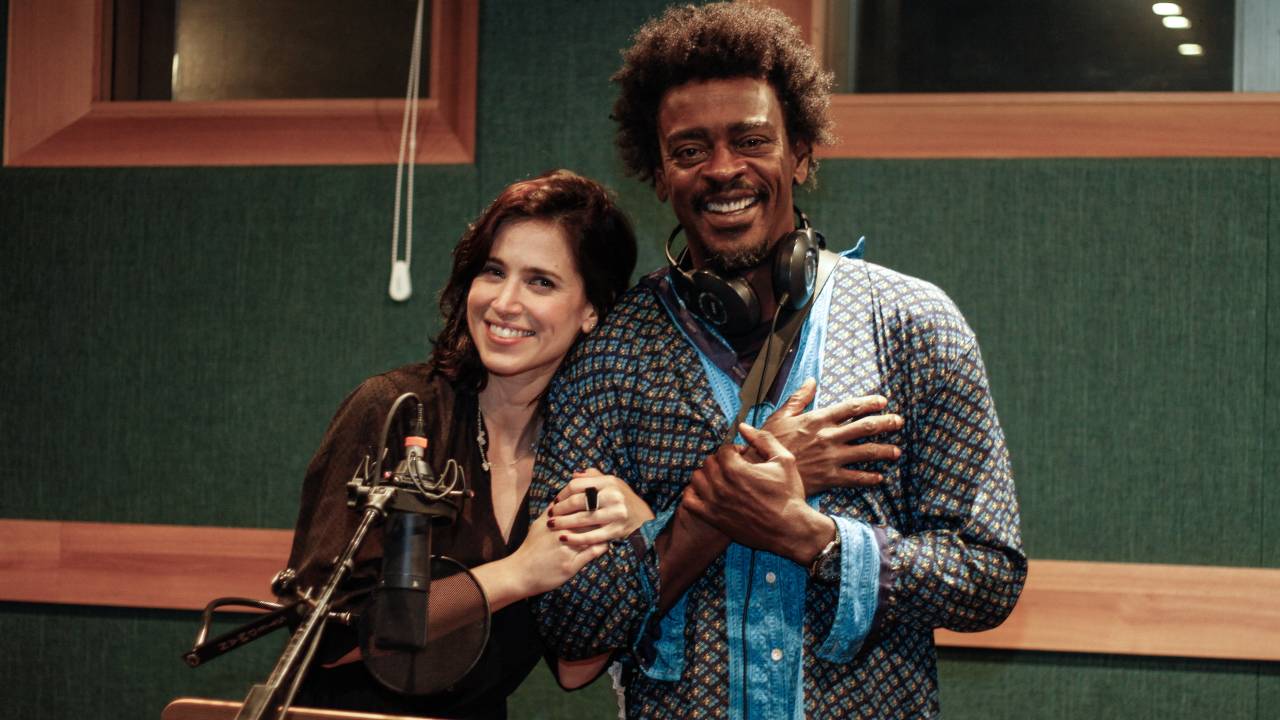 Mel Lisboa e Seu Jorge abraçados num estúdio de gravação de áudio