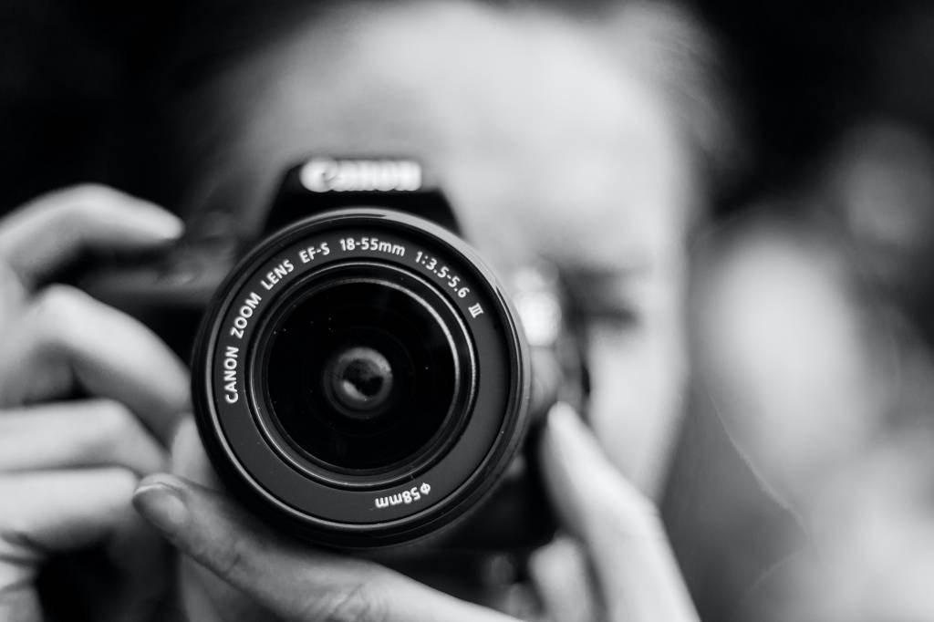 Fotógrafa com a câmera posicionada em frente ao rosto, em preto e branco