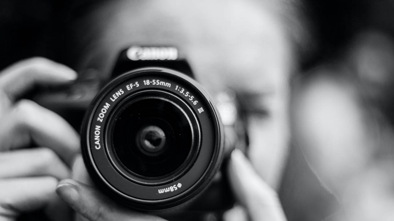 Fotógrafa com a câmera posicionada em frente ao rosto, em preto e branco