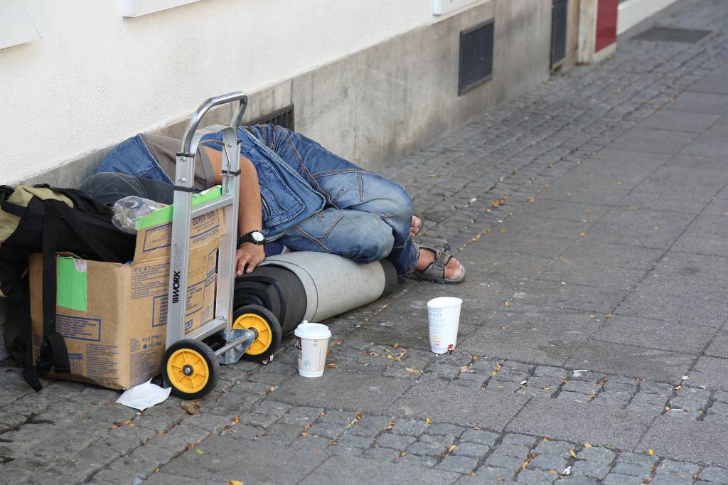 Imagem mostra pessoa em situação de rua deitada no chão e rodeada de objetos