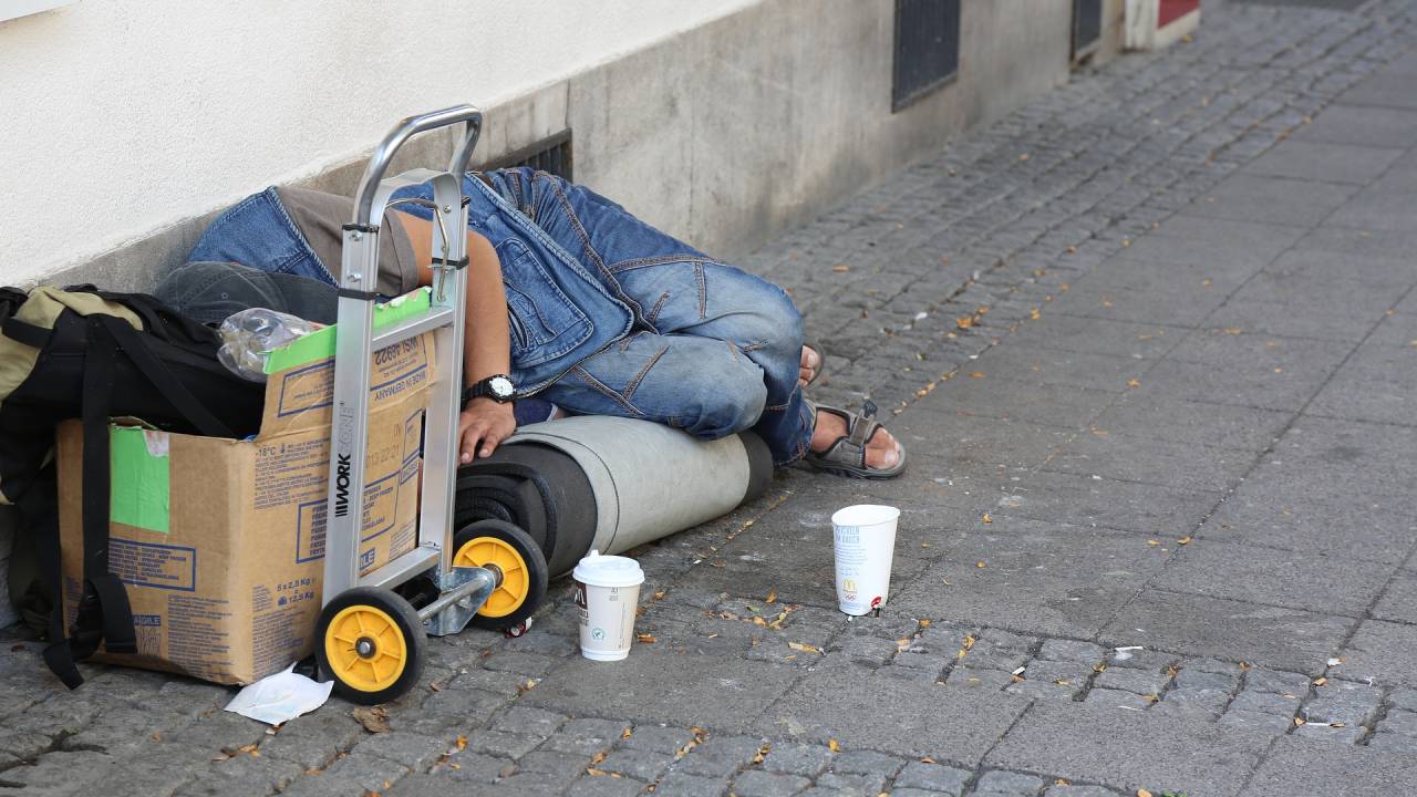 Imagem mostra pessoa em situação de rua deitada no chão e rodeada de objetos