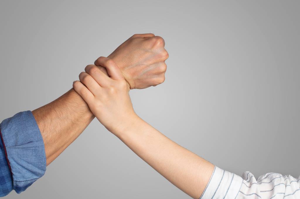 Uma mão detém um braço com o punho cerrado em gesto de agressão.