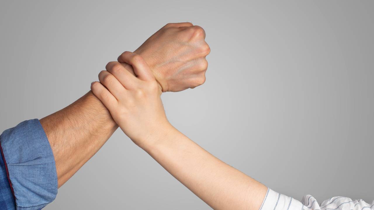 Uma mão detém um braço com o punho cerrado em gesto de agressão.