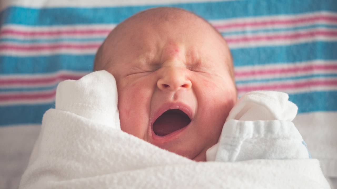Bebê recém nascido com a boca aberta e todo enrolado com manta branca