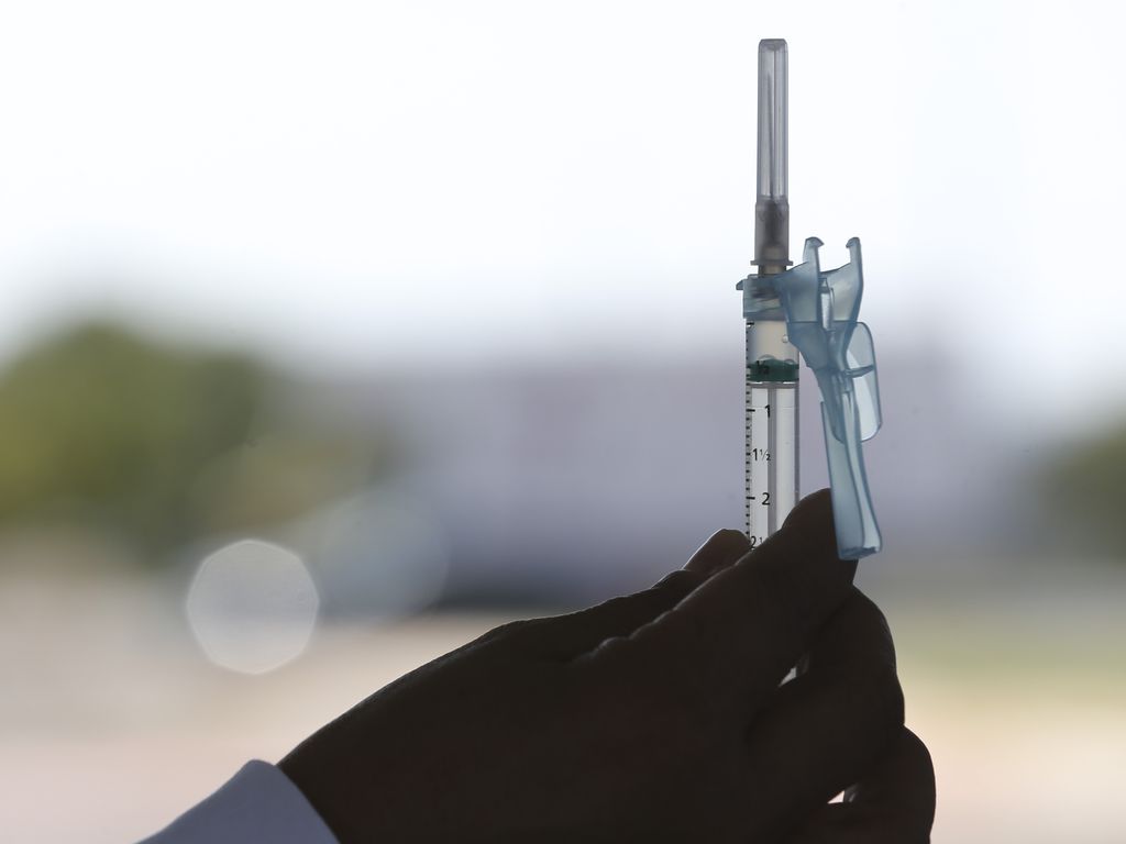 Imagem mostra pessoa segurando seringa da vacina