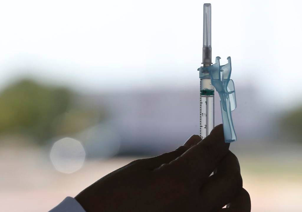 Imagem mostra pessoa segurando seringa da vacina