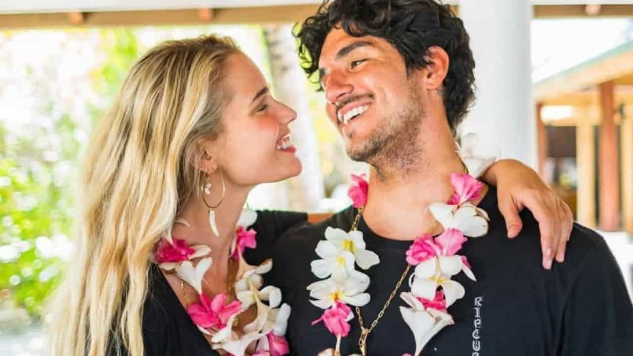 A imagem mostra Yasmin Brunet e Gabriel Medina, com flores no pescoço, se entreolhando e sorrindo