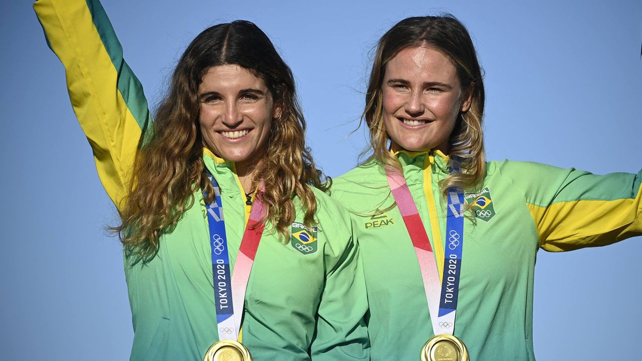 A imagem mostra Martine Grael e Kahena Kunze no pódio da Olimpíada, com a medalha de ouro no peito