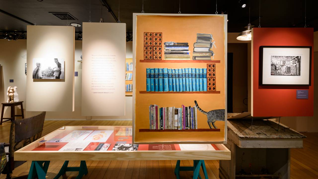 Exposição sobre Nise da Silveira no CCB, traz uma pintura de uma estante e uma mesa ao centro com alguns livros
