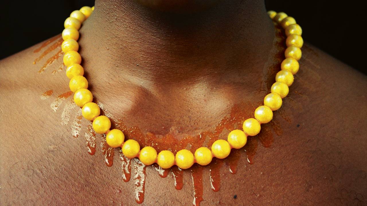 fotografia de homem negro, focalizando um dorso nu, com colar de contas amarelas