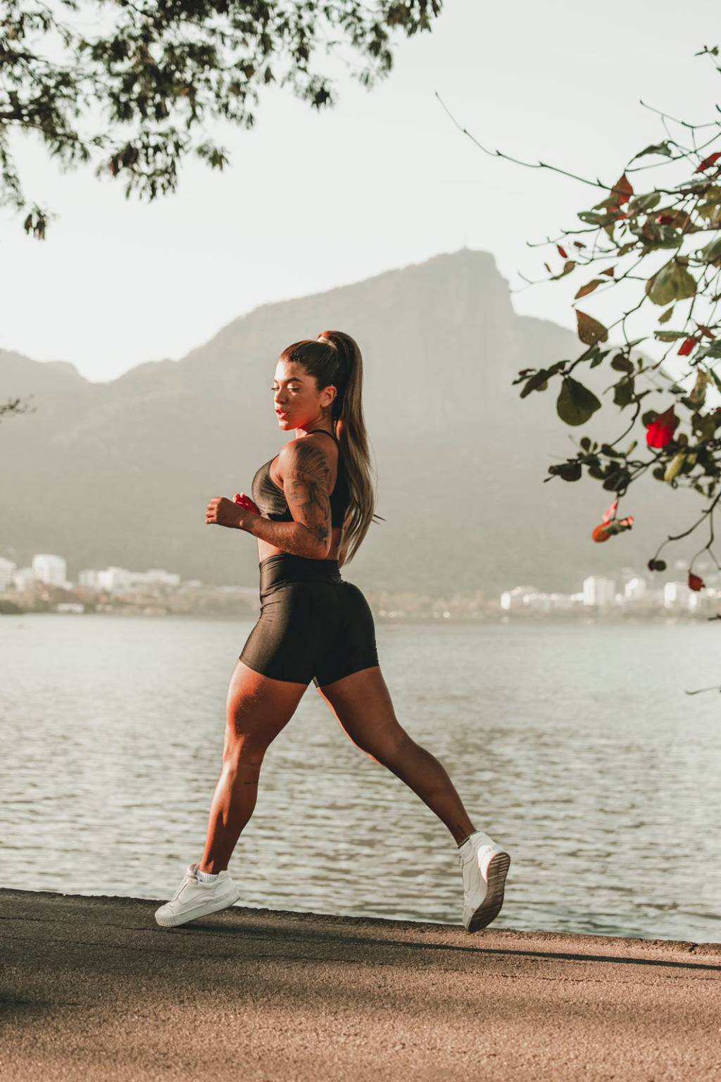 A imagem mostra uma mulher vestida de top fitness e short correndo em frente à Lagoa