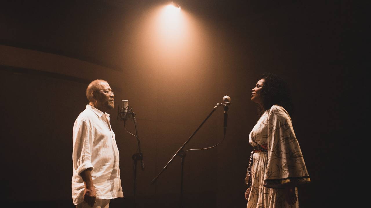 Martinho da Vila e Teresa Cristina, vestidos de branco, cantam ao microfone em um estúdio