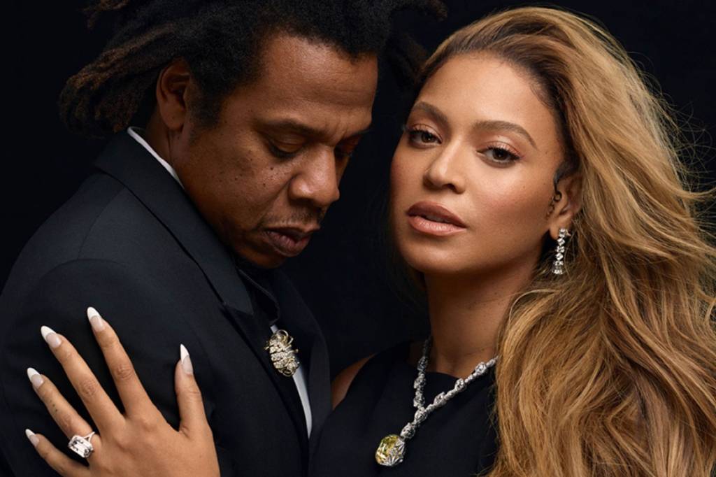 Jay-Z com olhos fechados abraça Beyoncé que olha para a câmera, e os dois usam vários diamantes da Tiffany & Co.