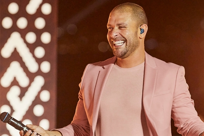 Diogo Nogueira, de roupa rosa, sorrindo, no palco, segurando microfone