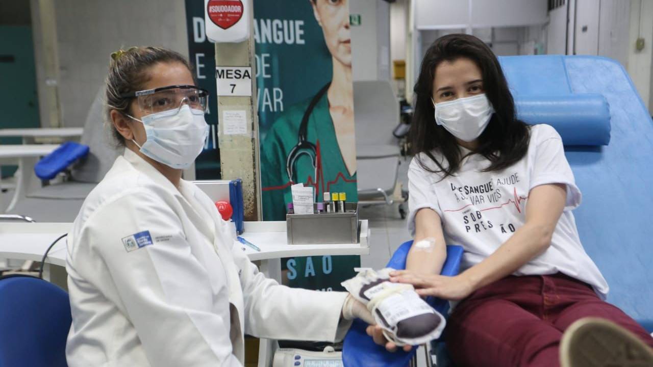 Foto mostra atriz Marjorie Estiano doando sangue ao lado de uma profissional de saúde