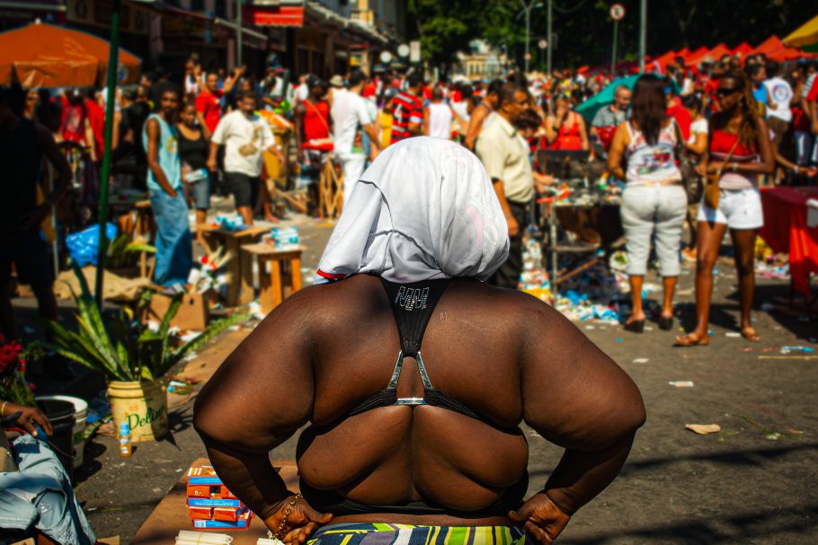 Uma mulher negra de costas, com as mãos na cintura e um pano na cabeça.