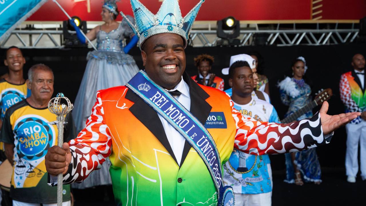 Foto mostra o escolhido a Rei Momo para o Carnaval de 2020 com terno colorido, faixa e coroa prateada