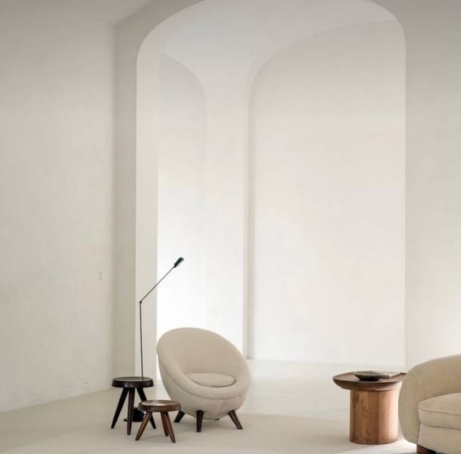 A imagem mostra uma sala com uma poltrona, banquinhos e uma luminária de piso