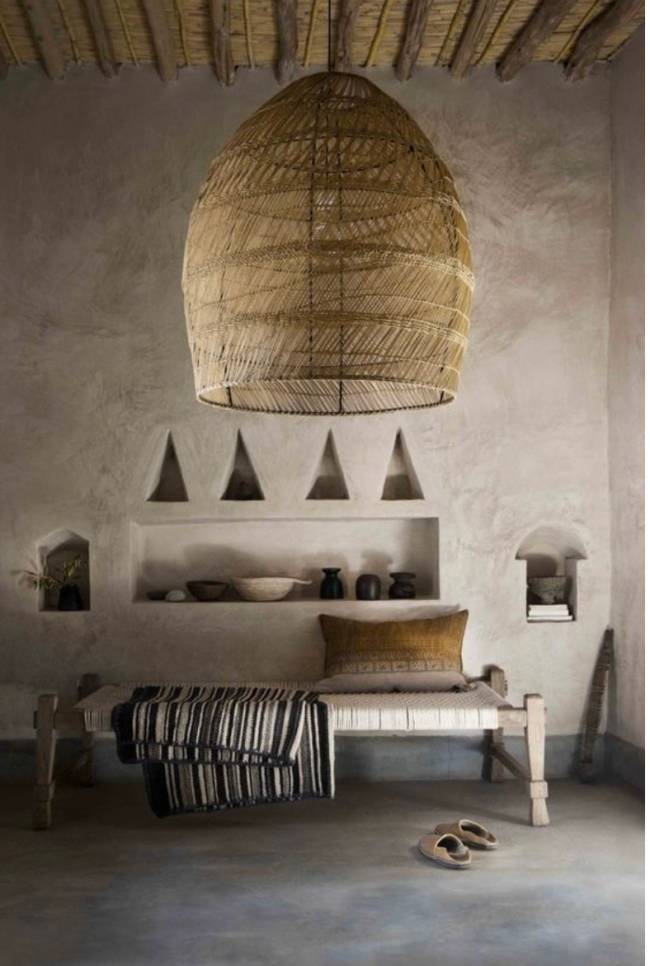 A imagem mostra uma sala com lustre de palha, banco e almofada