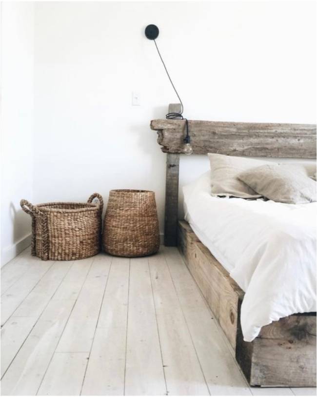 A imagem mostra um quarto com cestas de palha no chão, cama de madeira e parede branca