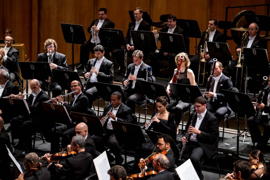 Músicos da Orquestra Petrobras Sinfônica sentados tocando seus instrumentos