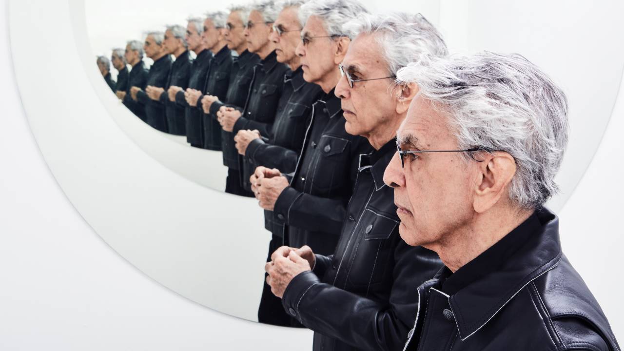 Caetano Veloso de perfil, de jaqueta preta, com sua imagem refletida e multiplicada por espelhos