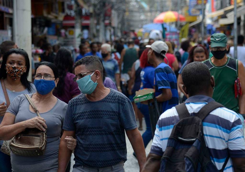 A imagem mostra pessoas de máscara andando por uma rua cheia de gente