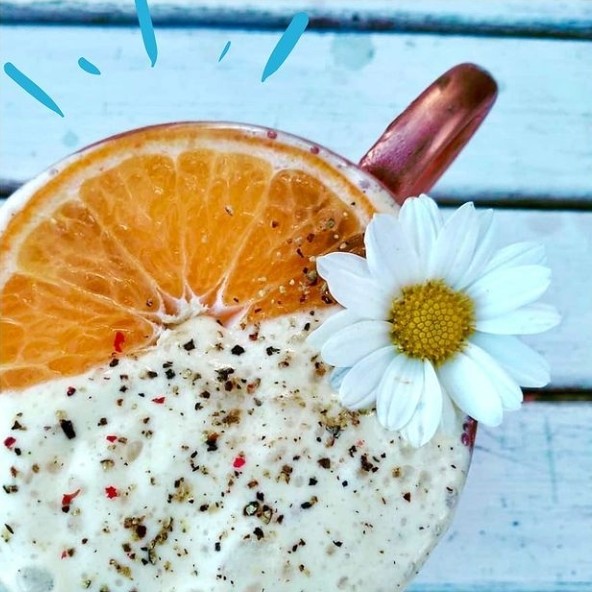 Foto mostra bebida Moscow Mule vista de cima, enfeitada com metade deuma laranja e uma pequena flor branca