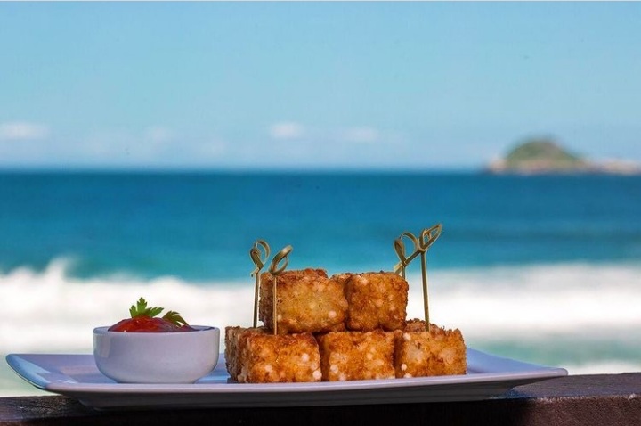 Foto mostra prato com dadinhos de tapioca e a vista da praia ao fundo