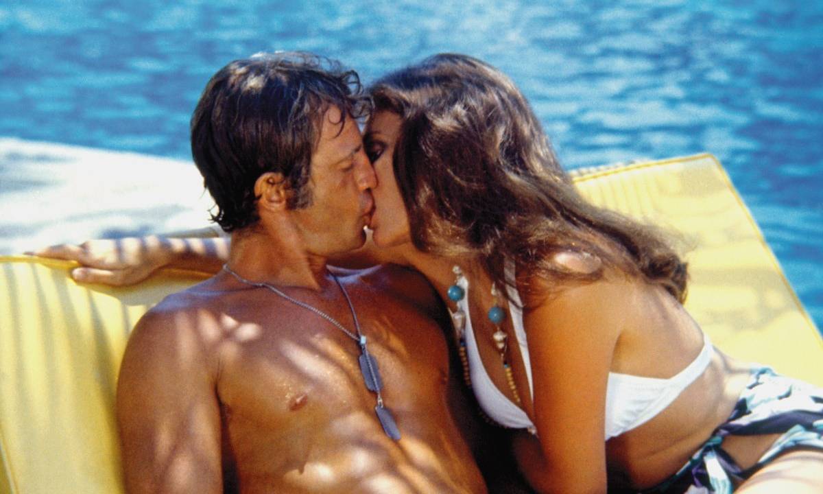 O ator Jean-Paul Belmondo e atriz Jacqueline Bisset se beijando à beira de uma piscina, no filme O Magnífico