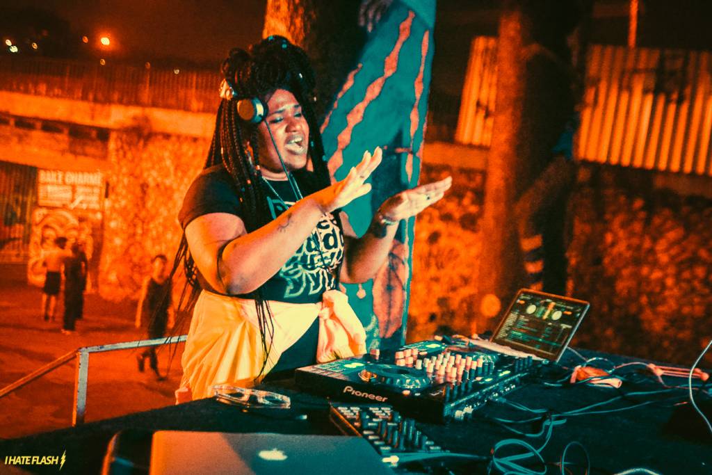 Foto mostra mulher negra com tranças tocando música como DJ