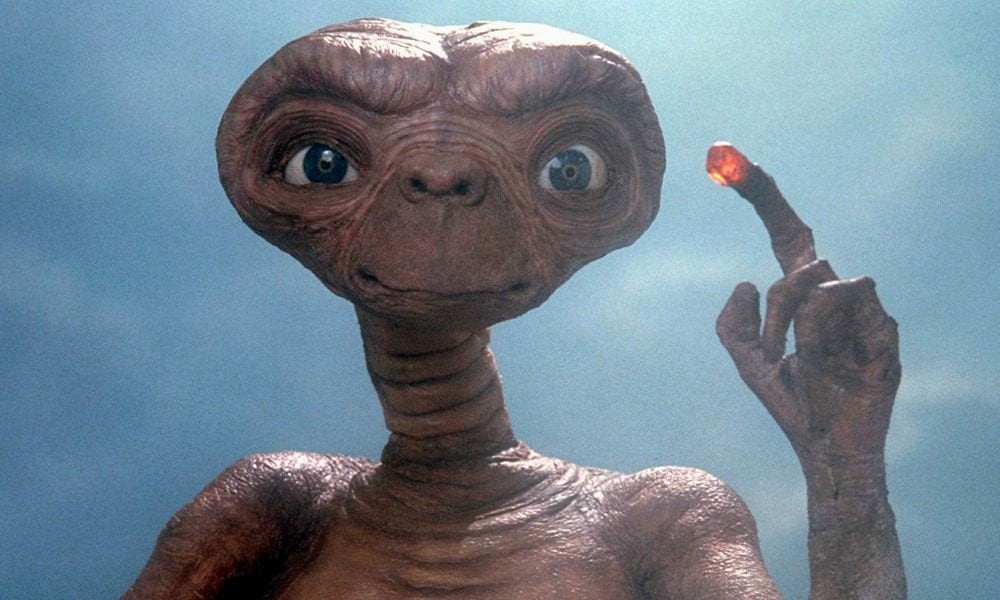 Cena do personagem principal do filme E.T. com ele com o dedo aceso levantado