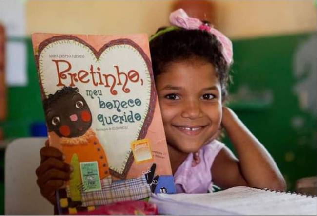 Foto de uma menina negra lendo seu livro na escola