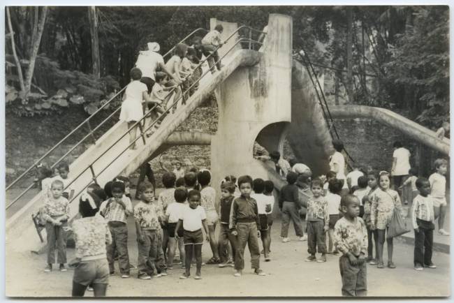 Imagem preto e branco mostra crianças brincando em escorrega