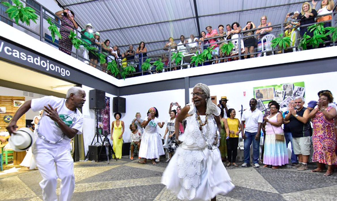 Foto mostra dois idosos negros com roupas brancas dançando o ritmo jongo
