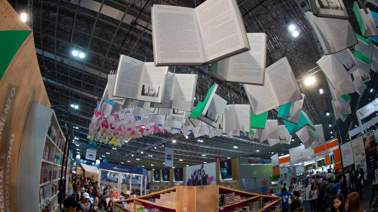 Foto mostra livros gigantes suspensos como decoração na Bienal do Livro