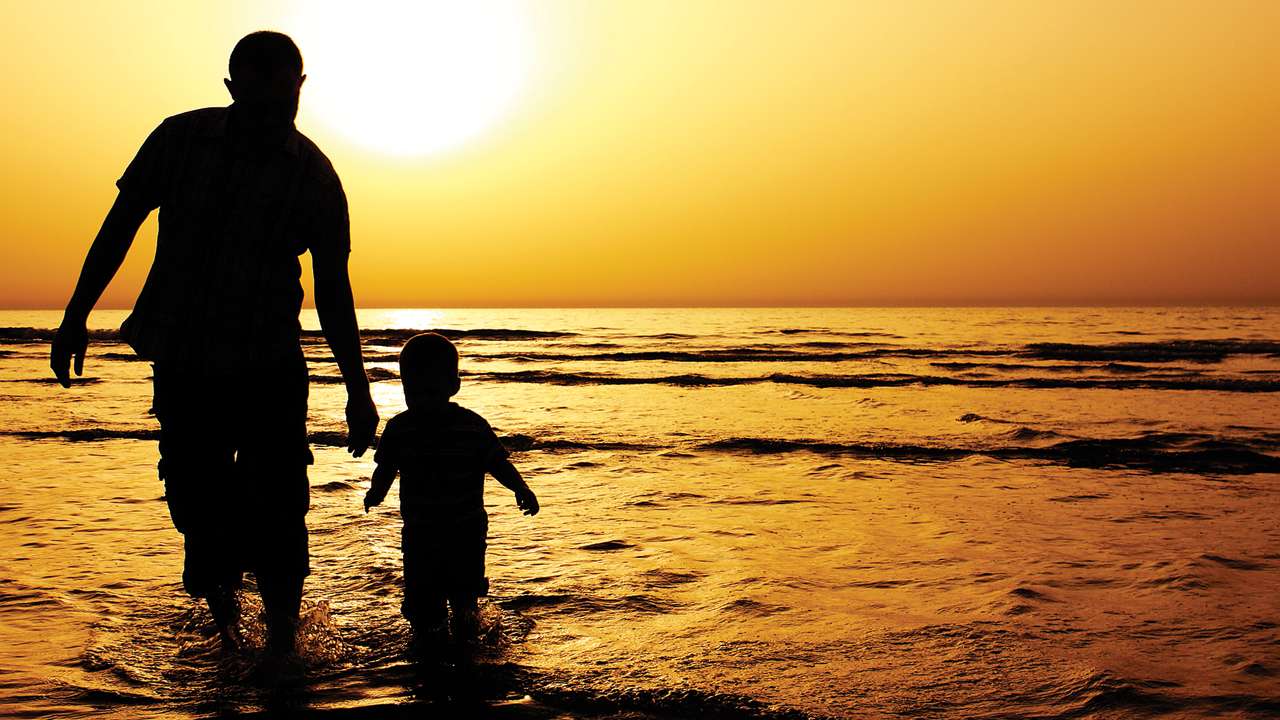 Pai e filho brincam no mar ao por do sol.