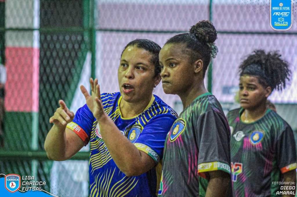 Foto mostra treinadora de futsal explicando tática para aluna