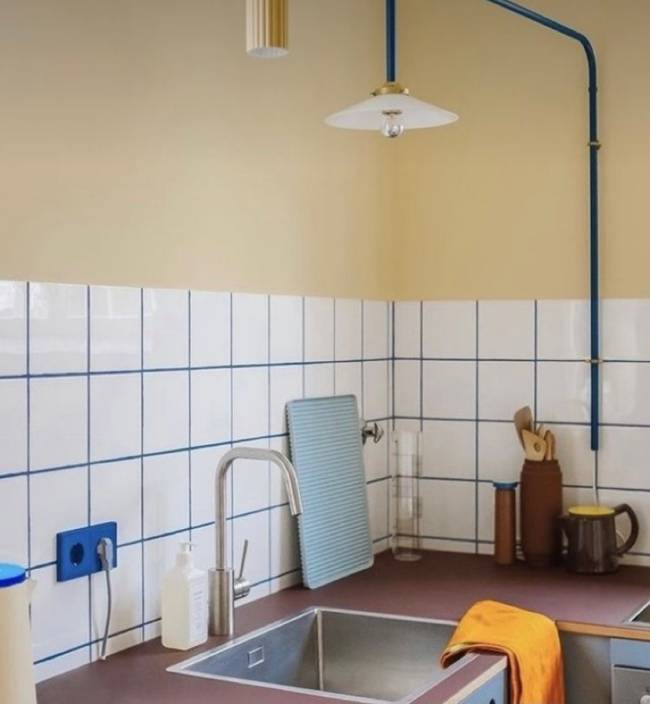 A imagem mostra uma cozinha com revestimento branco e rejunte azul