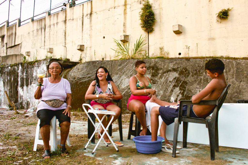 Foto mostra pessoas na comunidade sentadas em cadeiras