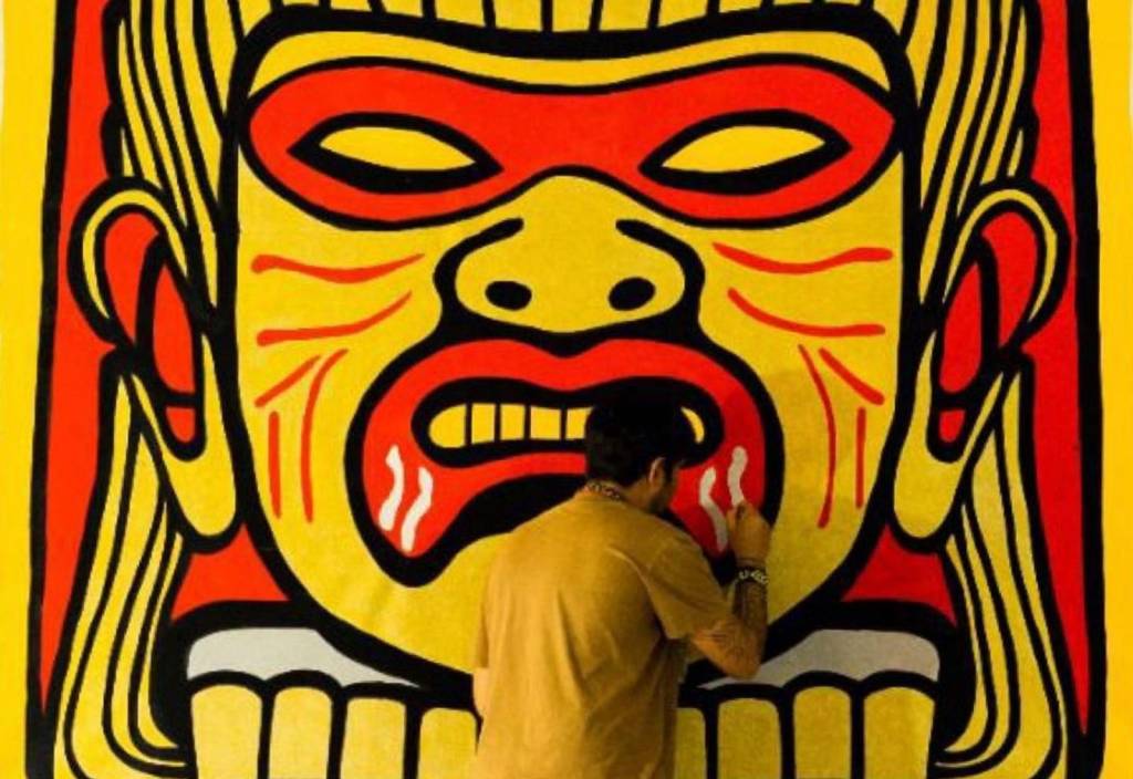 Foto mostra artista pintando uma obra de arte retratando um indígena
