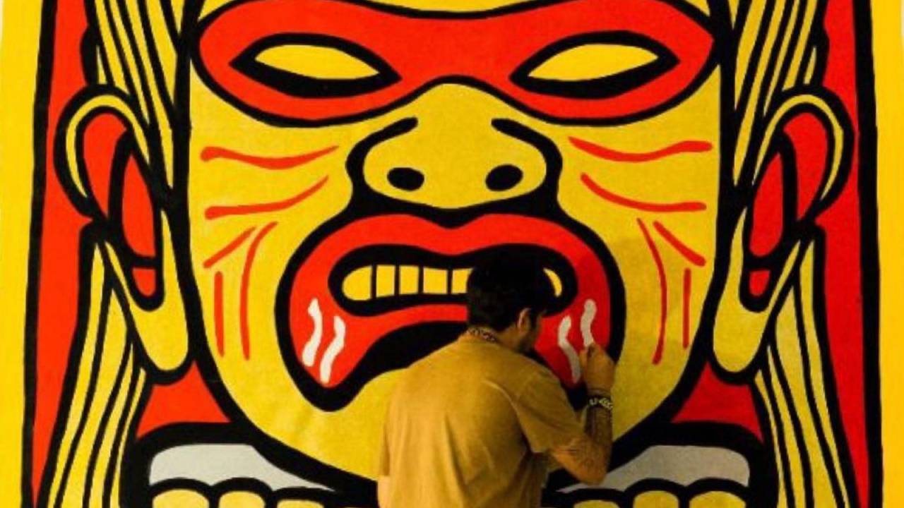 Foto mostra artista pintando uma obra de arte retratando um indígena