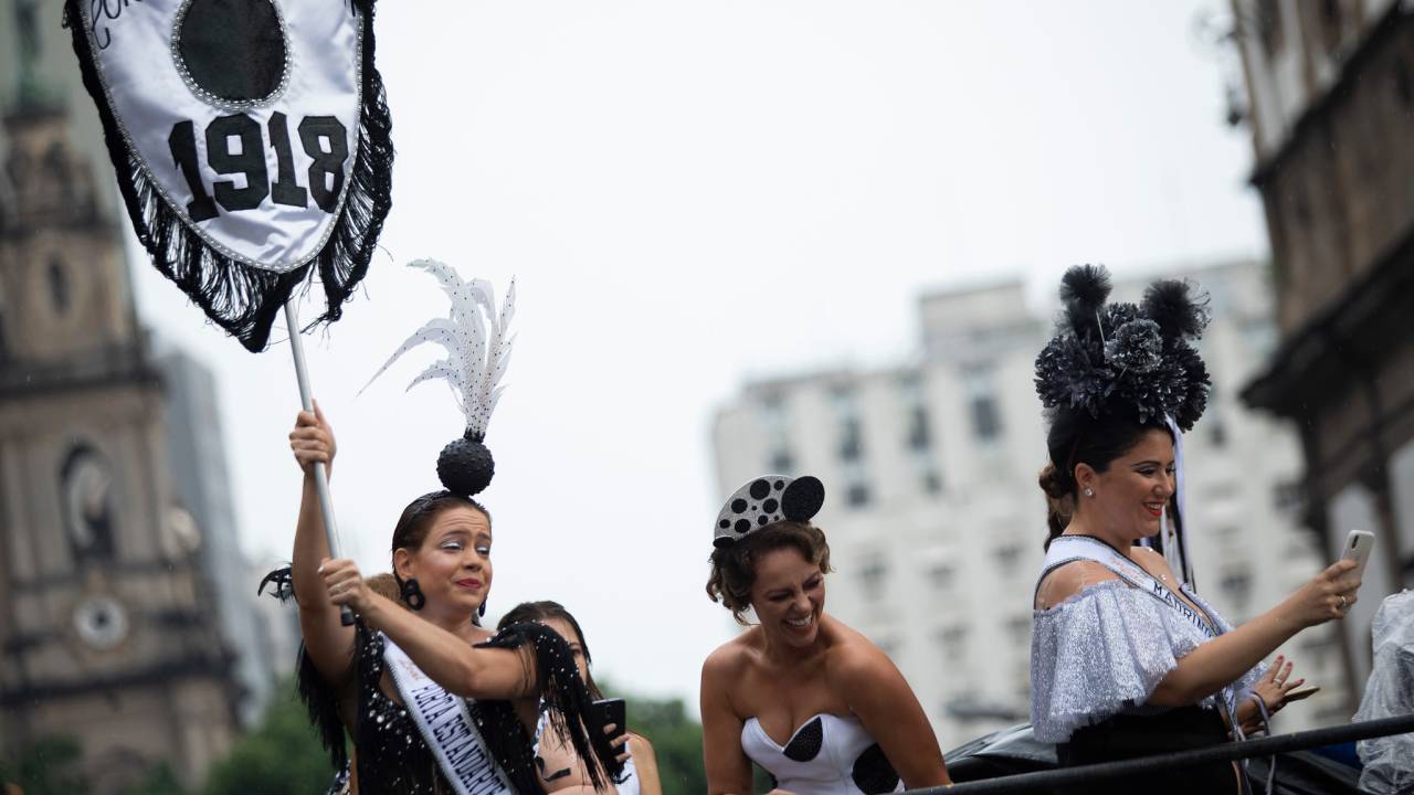 A atriz Leandra Leal, com o estandarte; a atriz Paolla Oliveira e a cantora Maria Rita no trio durante desfile do Cordão da Bola Preta. As três usam roupas pretas e brancas, com arranjos na cabeça nas mesmas cores.
